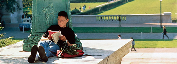 A Columbia University student leans against a sculpture atop the Low Library steps and reads.